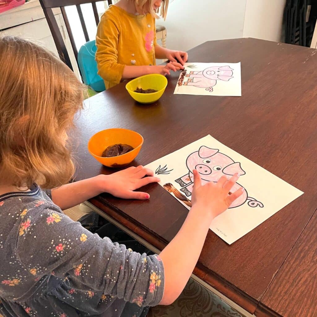 2 kids painting with chocolate pudding on a pig template for an easy farm craft