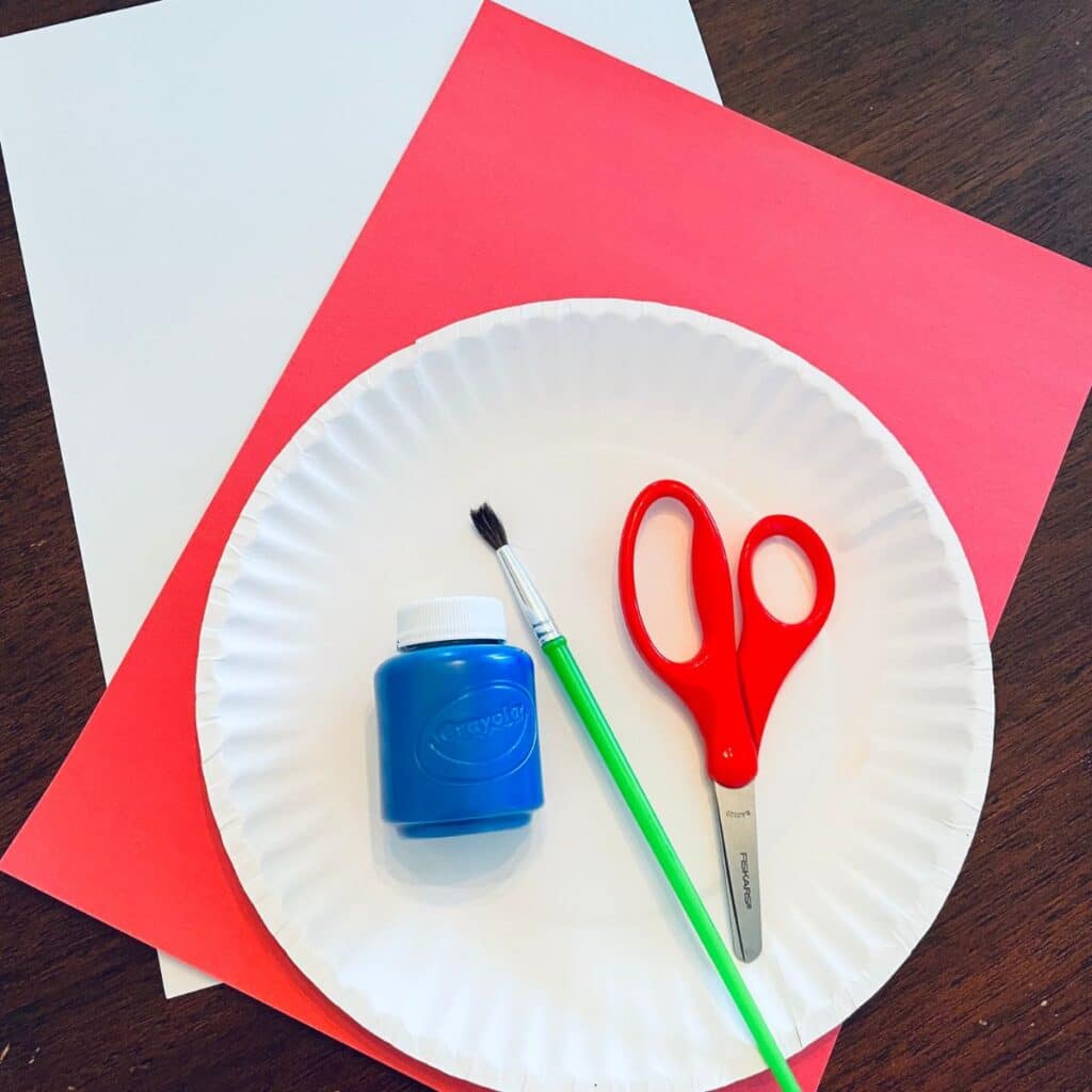 handprint flag craft supplies including white and red construction paper, blue paint, brush, and scissors.