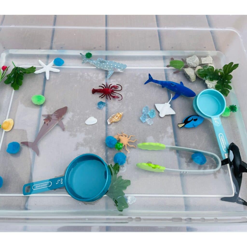 ocean sensory play idea - container filled with water, sea creatures, pom poms, gems, rocks, and more!