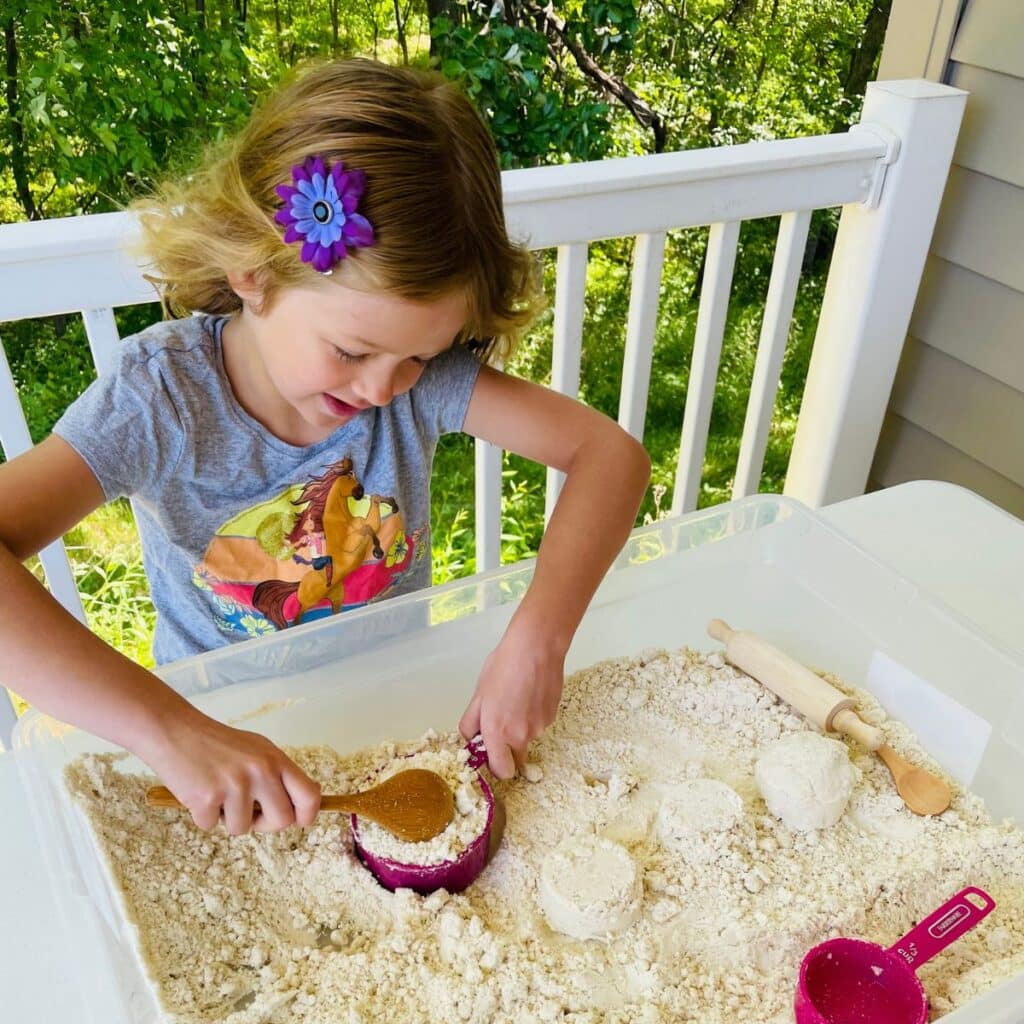 child on a porch outside play in moon sand sensory bin