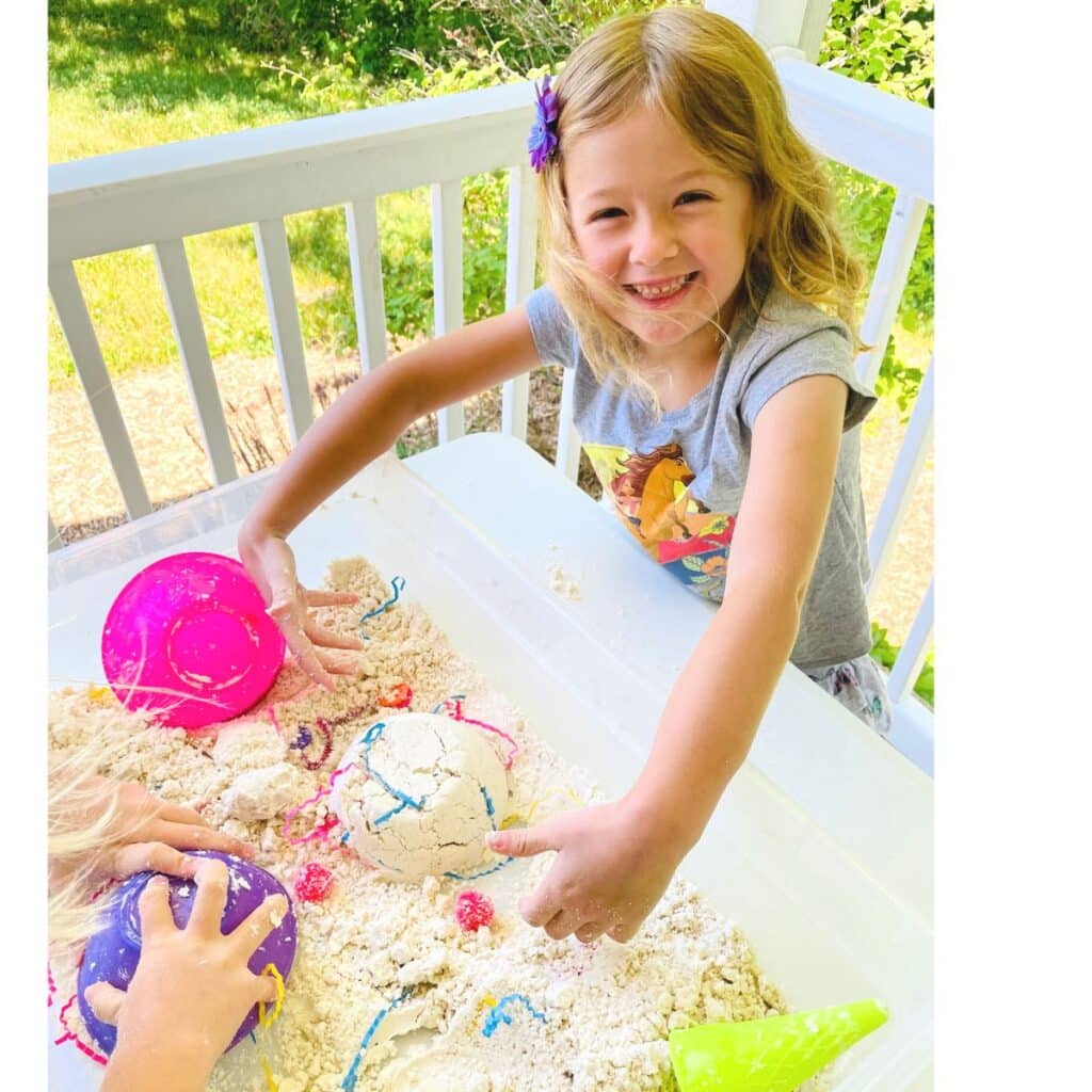 child smiles as she plays in summer sensory bin 