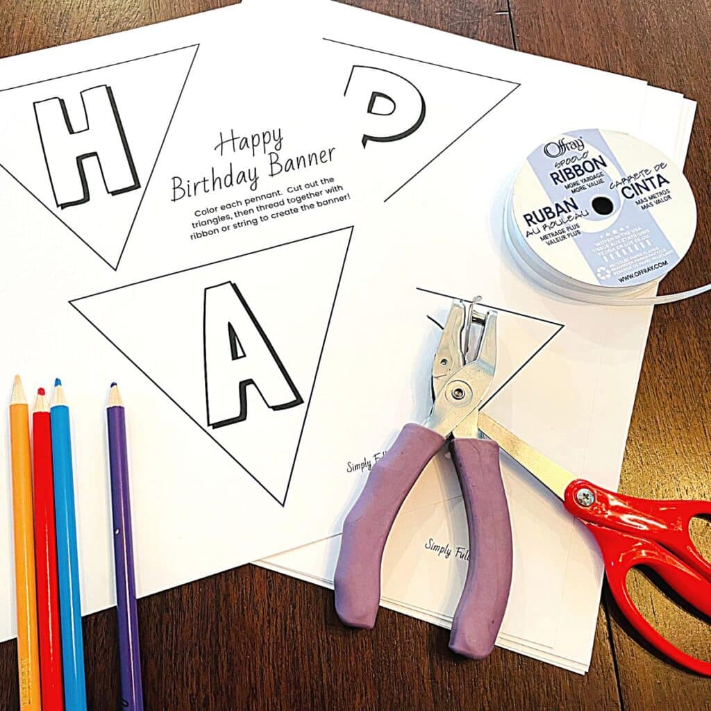 birthday banner supplies including black and white birthday banner printable, hole puncher, scissors, ribbon, and colored pencils.