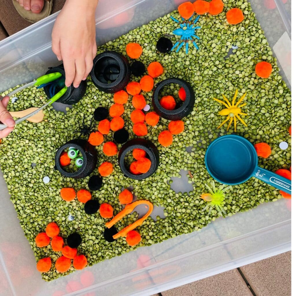 Halloween Sensory bin with pom poms, green split peas, googly eyes, plastic spiders, black caldrons and more!