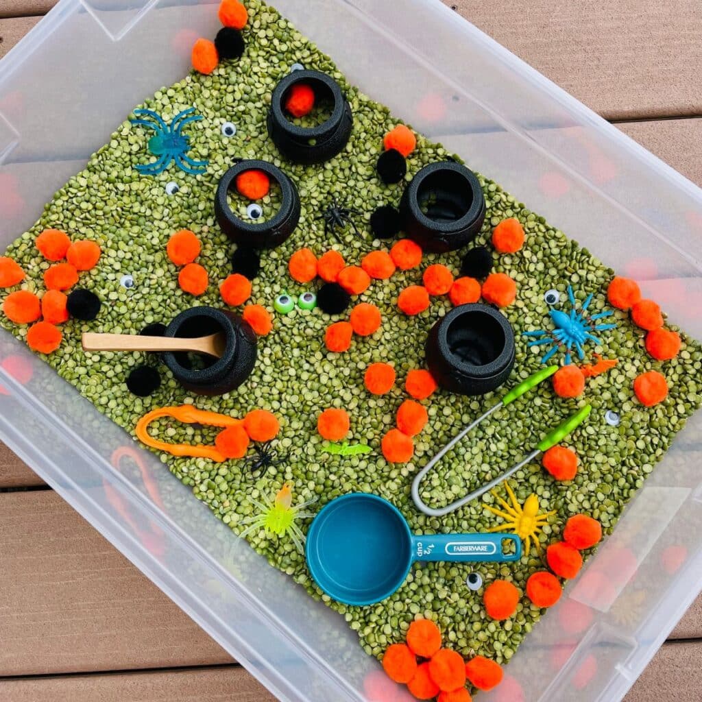 Halloween Sensory bin - Monster Stew with pom poms, green split peas, googly eyes, plastic spiders and bugs, caldrons and more!