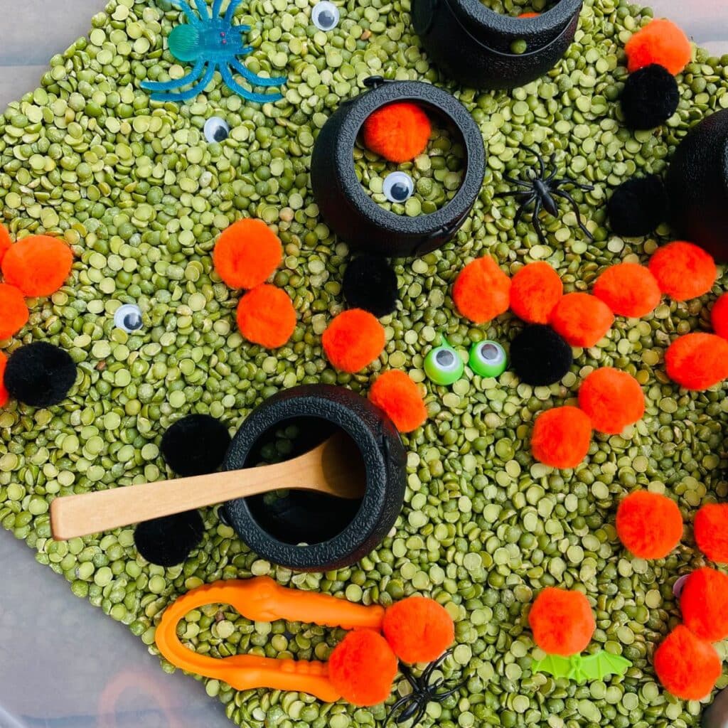 Monster Stew Halloween Sensory bin - pom poms, green split peas, googly eyes, plastic spiders and bugs, caldrons and more!