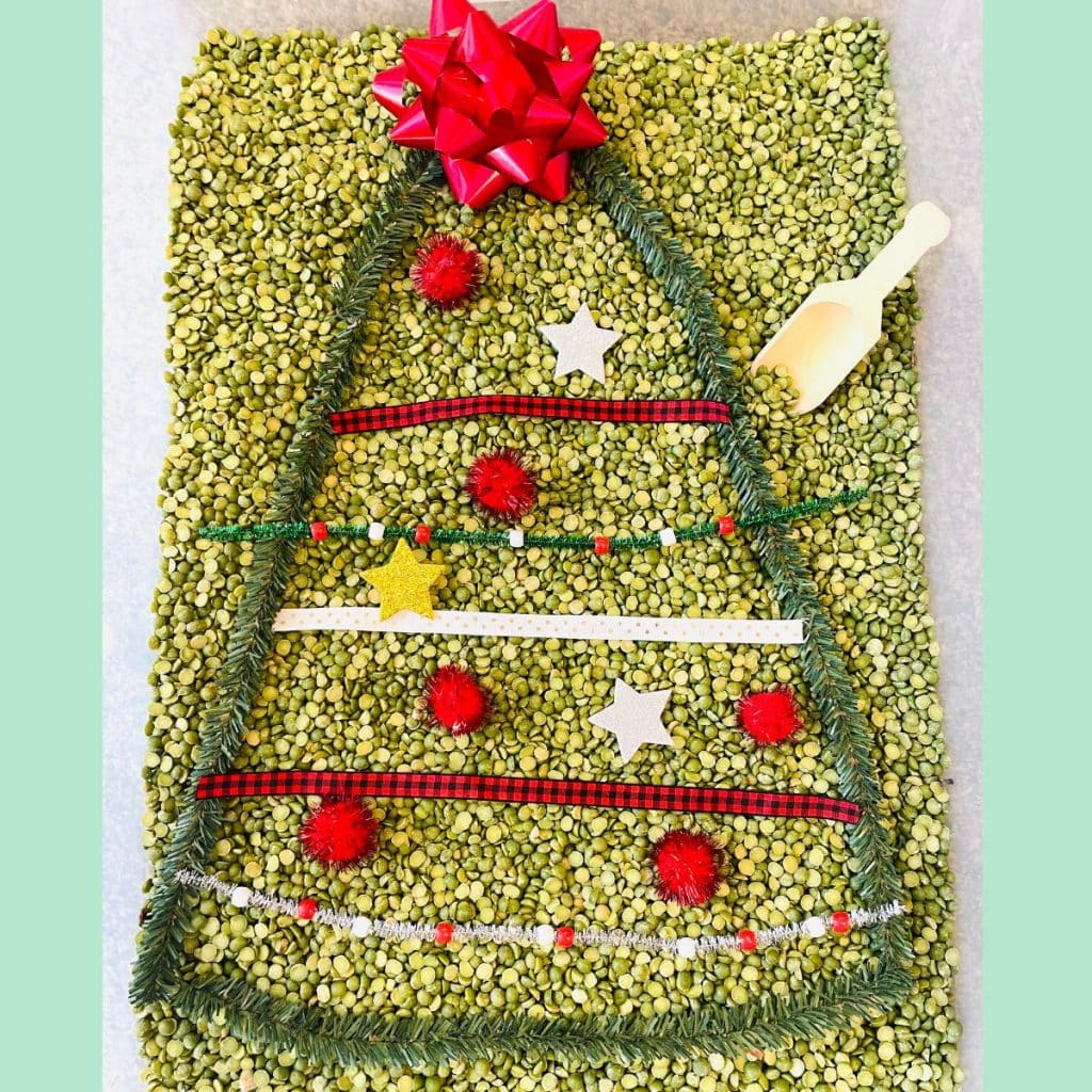 Christmas sensory bin - green split peas with greenery branches to form a Christmas tree decorated with pom poms, ribbon, and more.