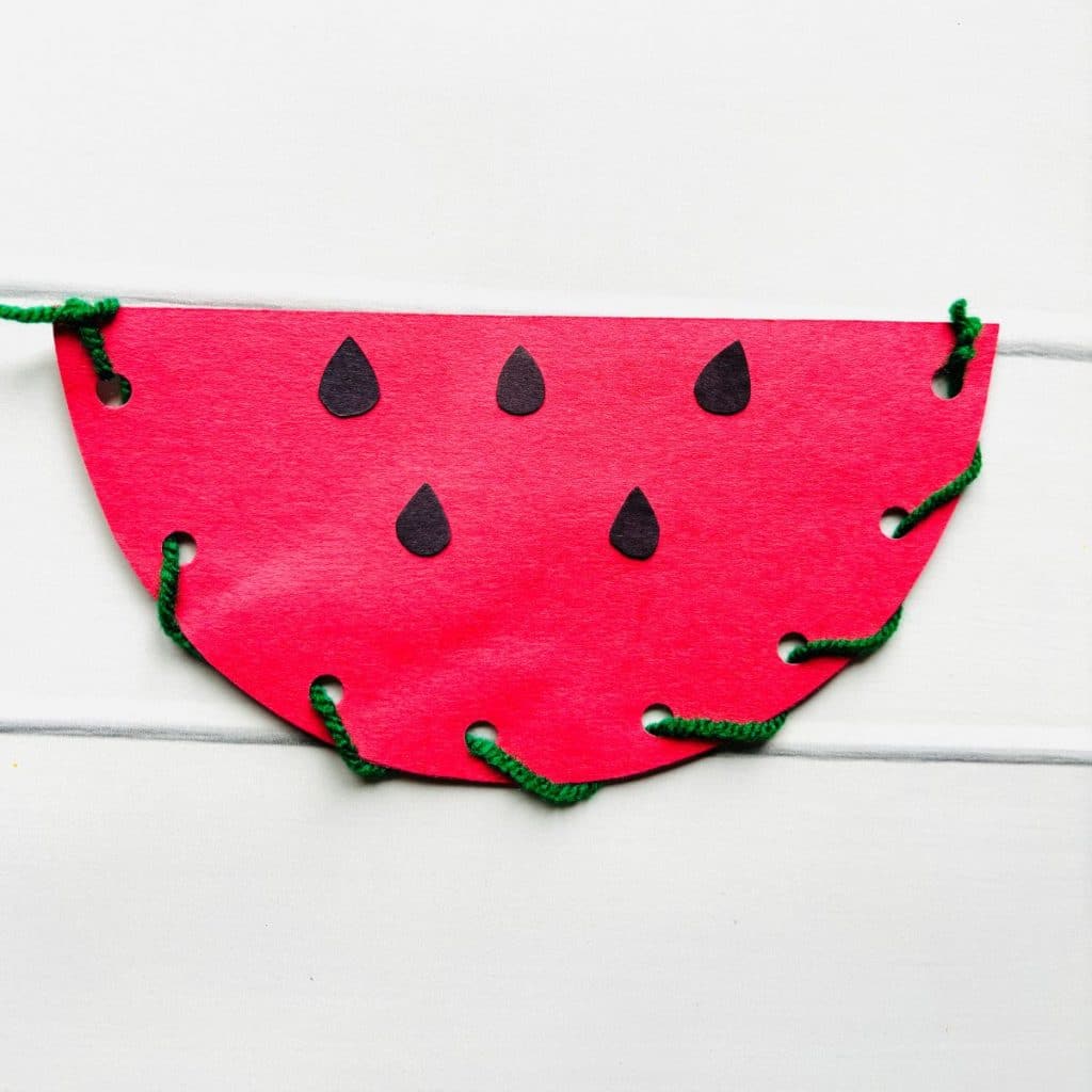 paper watermelon craft  made with red construction paper, black paper seeds and green yarn laced around the edge.
