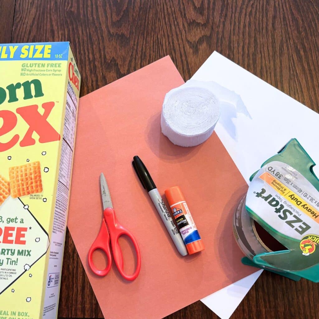 Supplies for DIY dog valentine box including tape, white card stock, brown construction paper, glue stick, black sharpie, white crepe paper, scissors, and cereal box